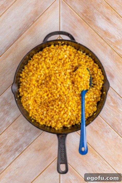 A spoon in a cast iron skillet of lightly browned, cooked fried corn.