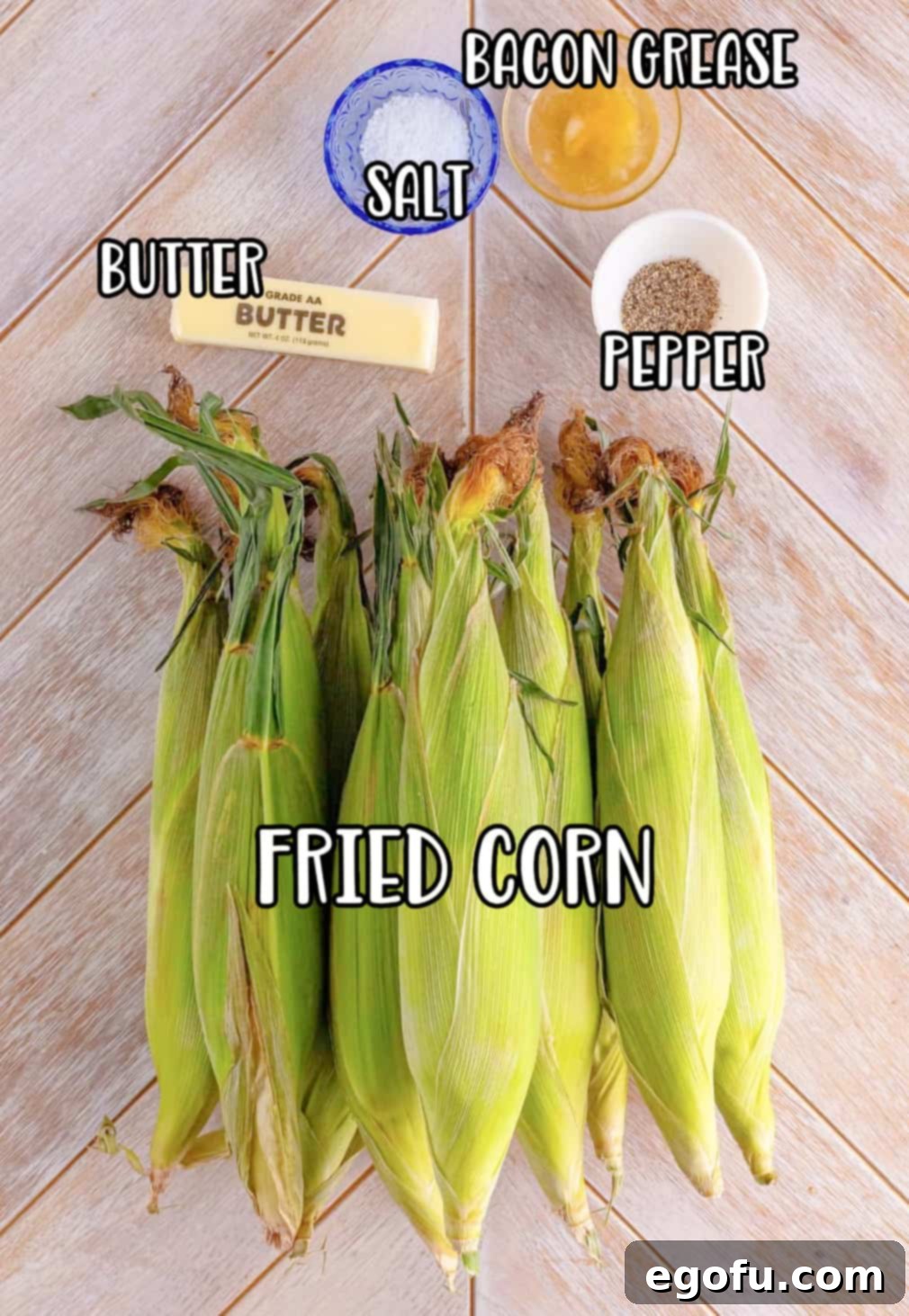 Fresh corn on the cob, a stick of butter, a container of bacon grease, and small bowls of salt and pepper on a rustic surface.