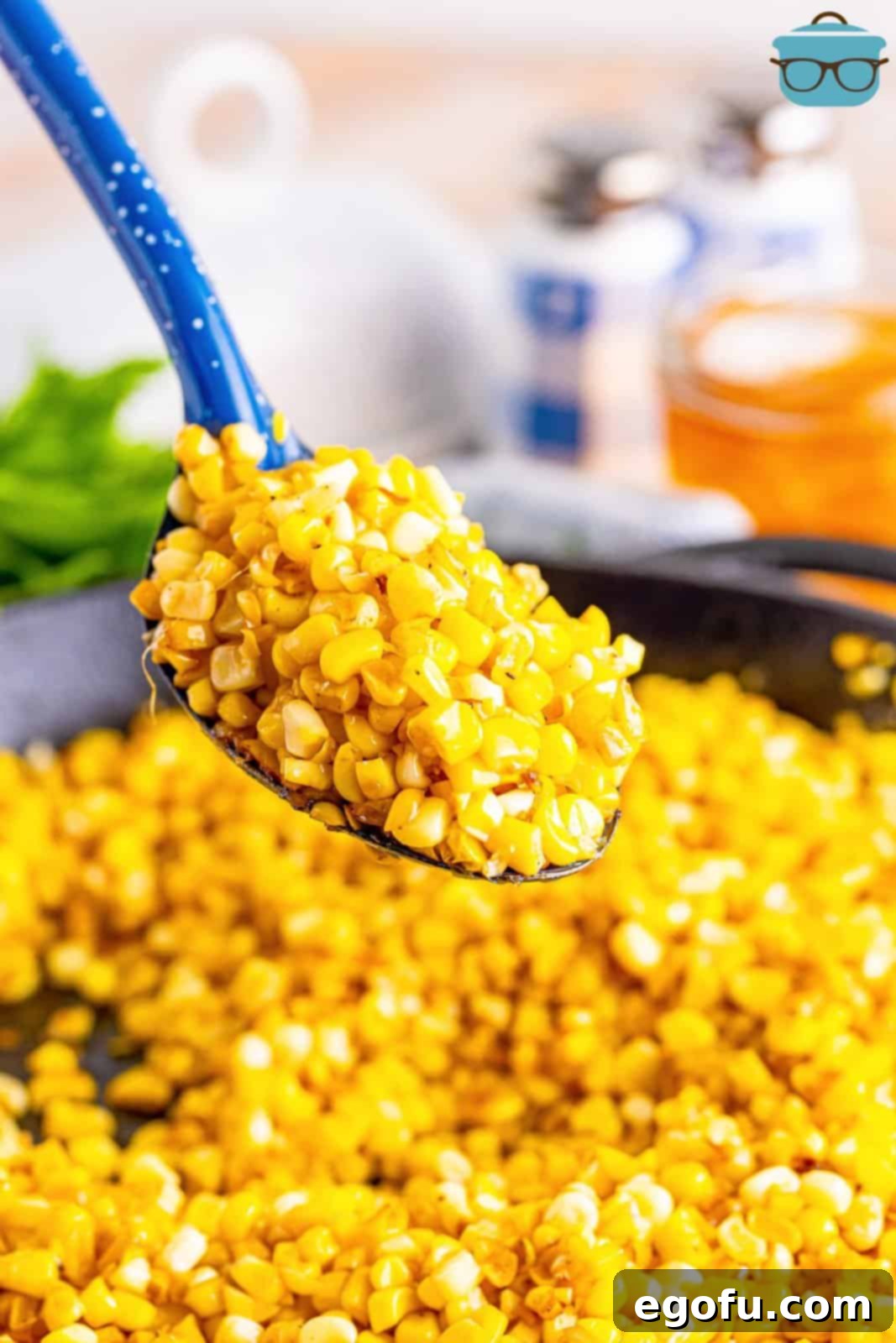 A serving spoon lifting a portion of golden Southern Fried Corn from a large cast iron skillet, ready to be served.