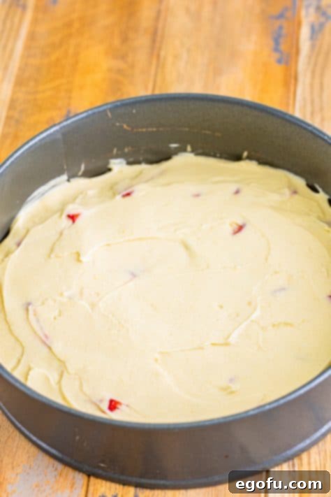 Cake batter on top of strawberry mixture in a springform pan.