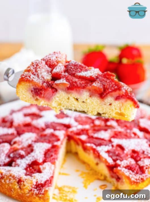 A slice of strawberry upside down cake on a serving utensil above the rest of the cake.