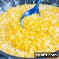 A blue serving spoon in a skillet of creamed corn.