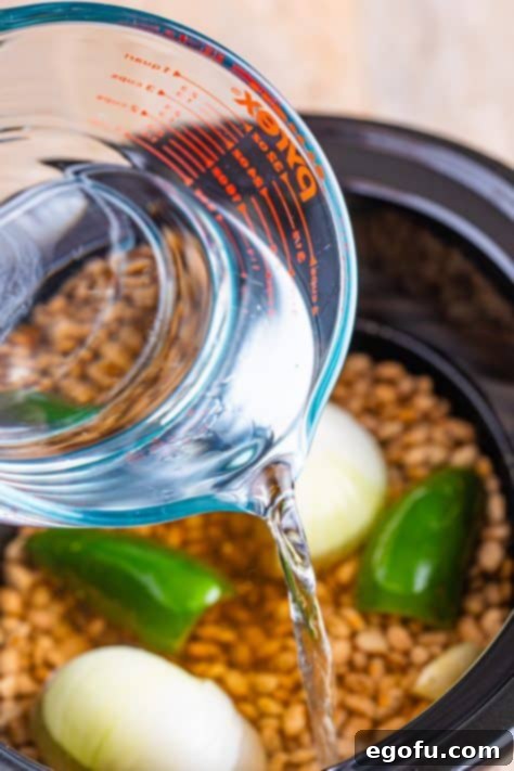 A measuring cup of water being poured in the Slow Cooker with other refried bean ingredients.