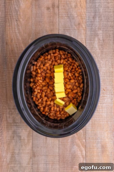 Drained and cooked beans with butter on top in a slow cooker.