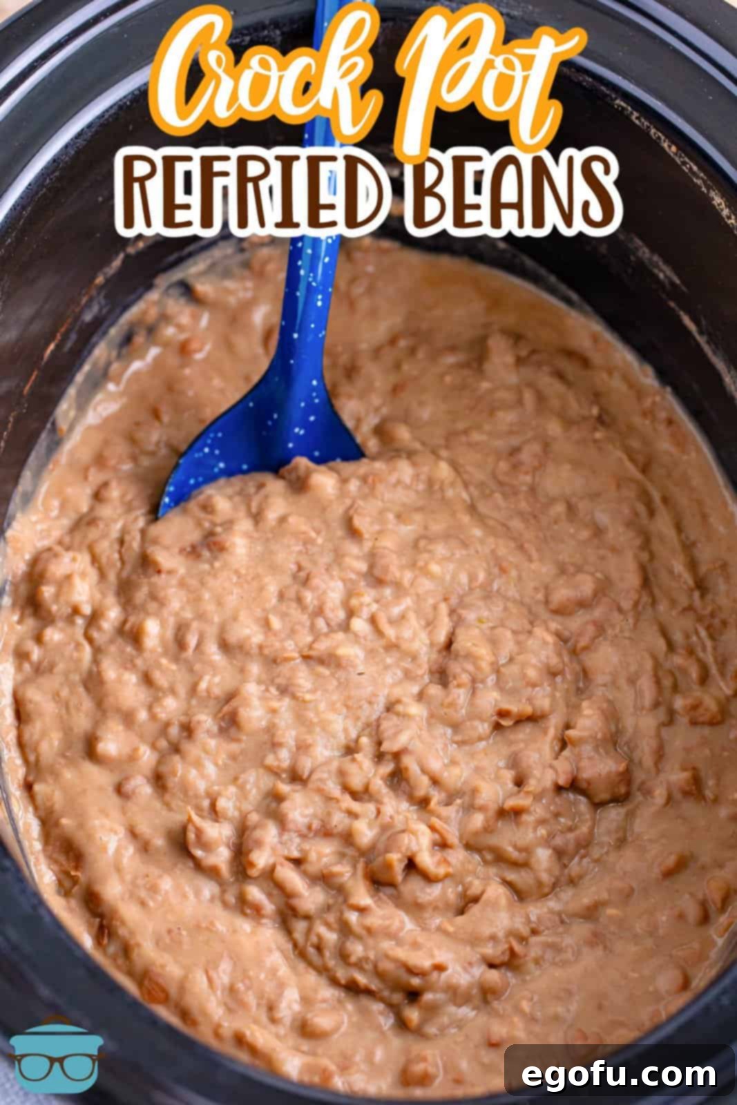 A blue serving spoon in a slow cooker of refried beans.