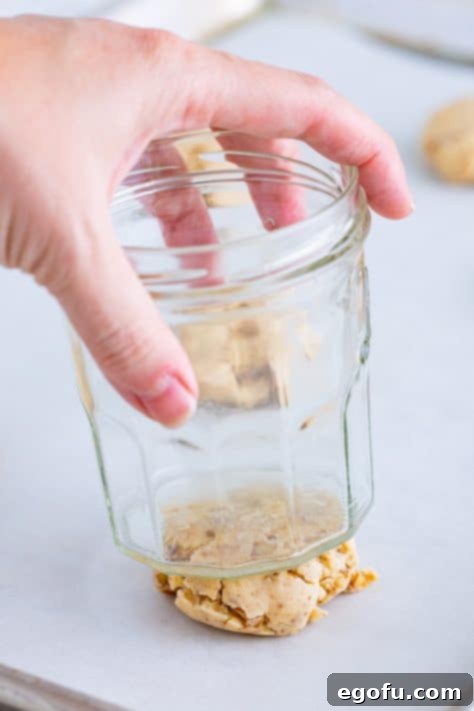 A glass pressing down on a Pecan Sandies cookie dough ball on a baking sheet to flatten it.