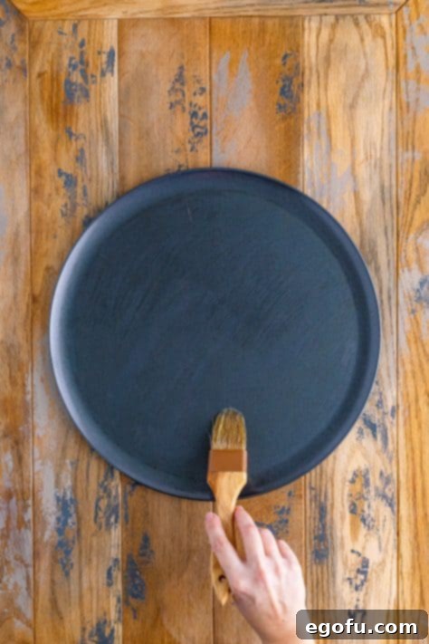Oil being brushed on a pizza pan with a pastry brush.