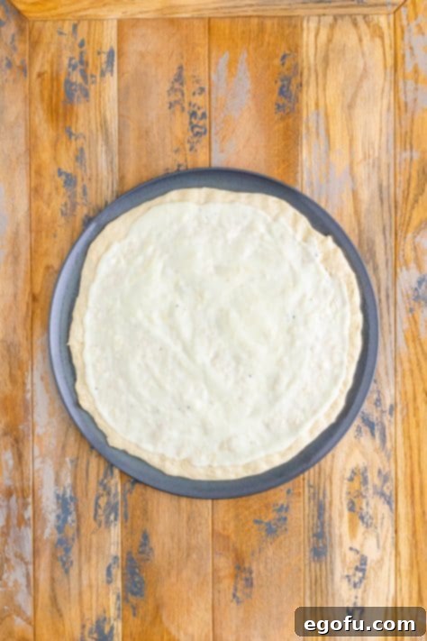 Pizza dough and white sauce on a pizza pan.