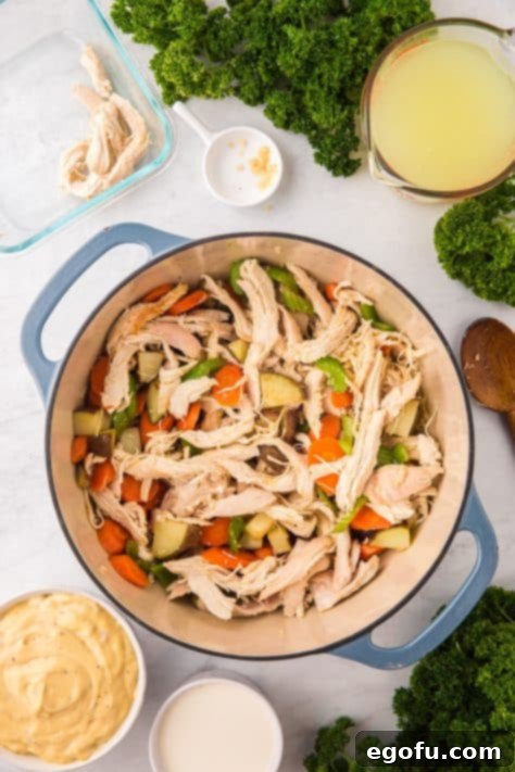 A pot with garlic, shredded chicken, diced carrots, celery, potatoes, and melted butter.