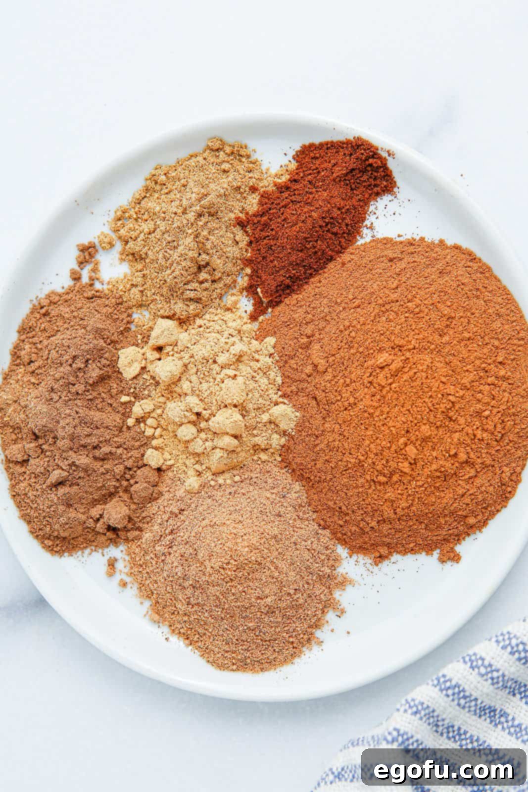Cinnamon, nutmeg, cardamom, allspice, ginger, and cloves arranged on a plate before mixing.