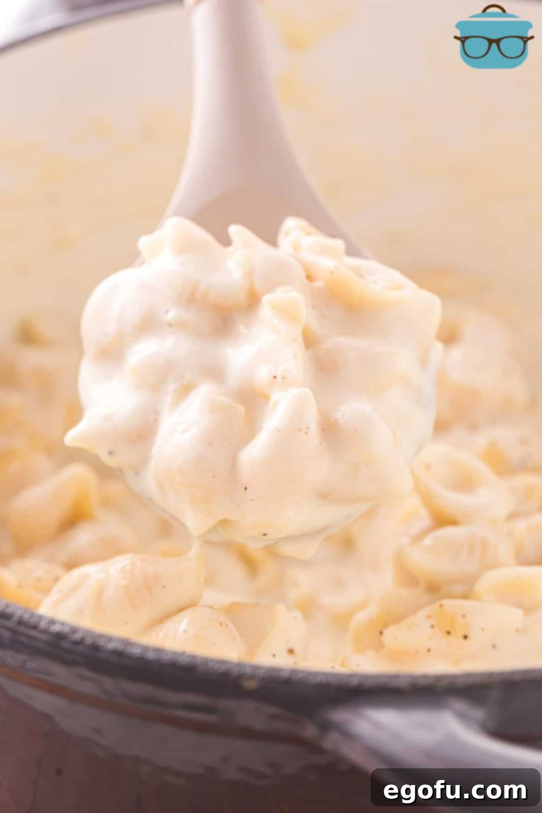 Panera's Signature Creamy Mac and Cheese 2 A wooden utensil holding a scoop of creamy white cheddar mac and cheese above the pot, highlighting its rich texture.