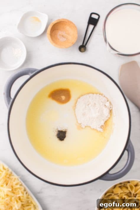 Panera's Signature Creamy Mac and Cheese 11 A large pot containing melted butter, flour, garlic powder, salt, and pepper, being whisked together.