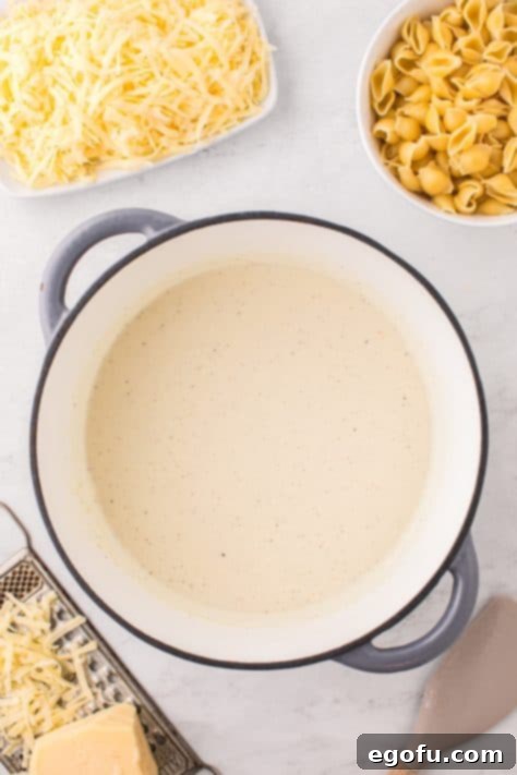 Panera's Signature Creamy Mac and Cheese 12 Milk being whisked into the roux mixture in a pot on the stove.