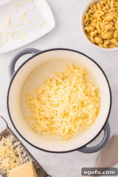 Panera's Signature Creamy Mac and Cheese 13 Shredded white cheddar cheese being added to the thickened sauce in a pot.