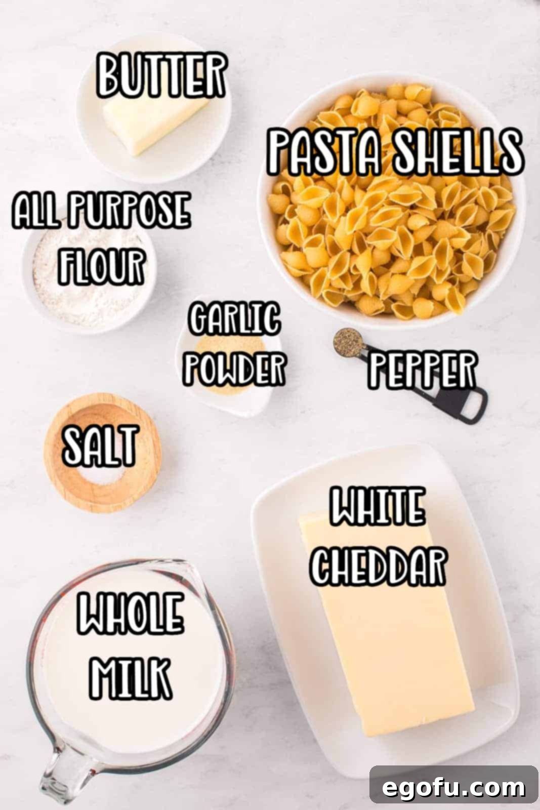 Panera's Signature Creamy Mac and Cheese 3 A vibrant flat lay showcasing all the fresh ingredients needed for homemade Panera Mac and Cheese: pasta shells, white cheddar cheese block, butter, all-purpose flour, garlic powder, salt, pepper, and a bottle of whole milk.