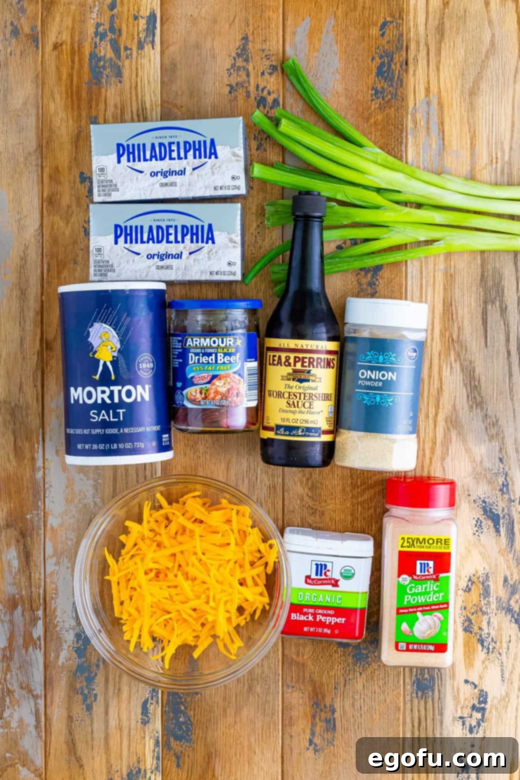 Savory Beef Cheese Delight 4 A vibrant flat lay showing all the essential ingredients for a dried beef cheese ball: cream cheese blocks, fresh green onions, shredded sharp cheddar cheese, a jar of dried beef, and small bowls of salt, garlic powder, onion powder, black pepper, and Worcestershire sauce.