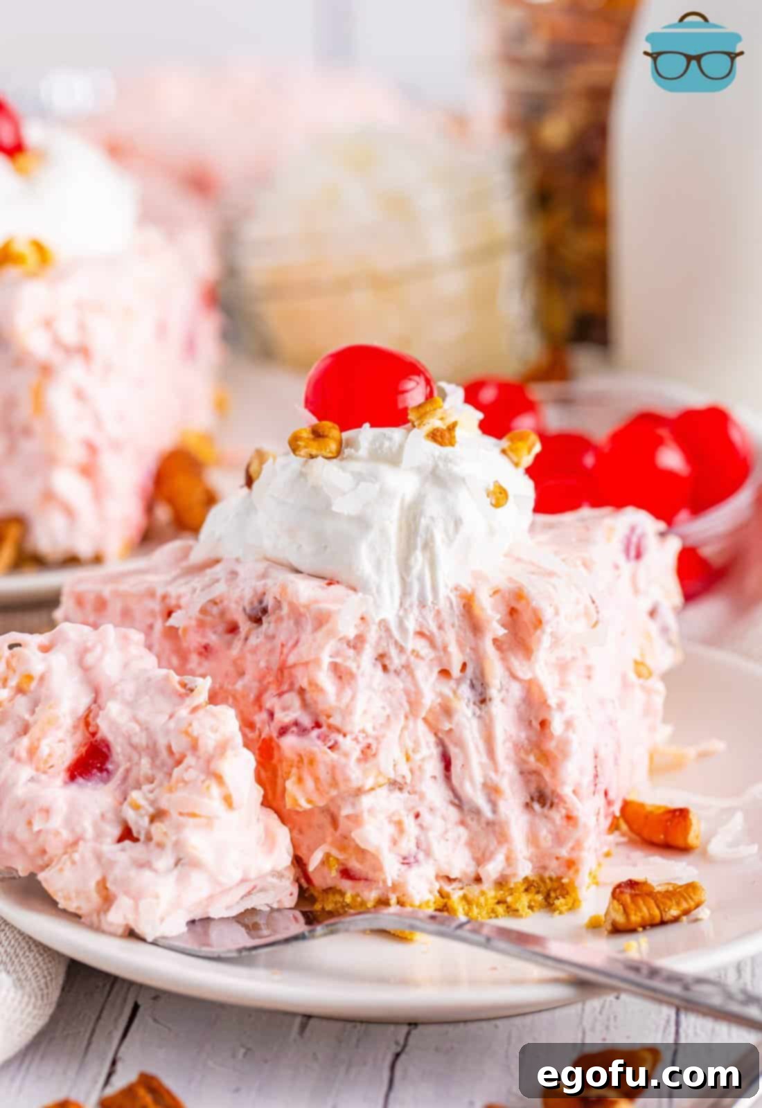 A perfectly sliced piece of Millionaire Pie, displaying its vibrant layers of pineapple, cherries, and coconut, with a small bite taken out, inviting a taste.