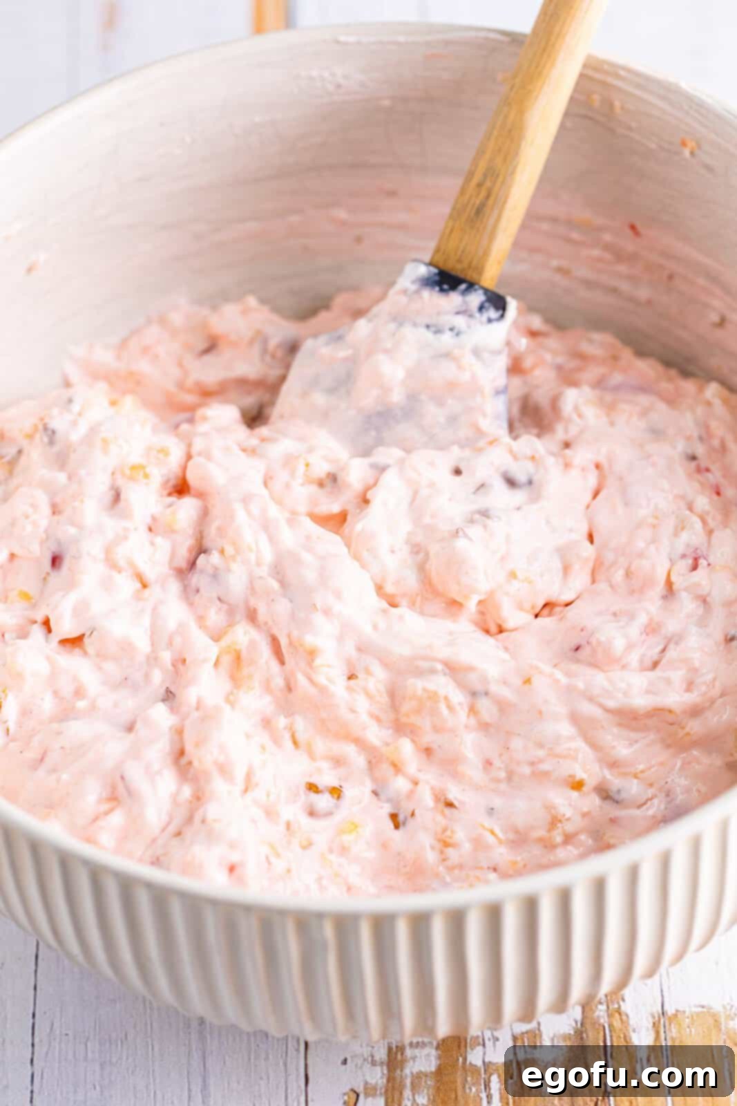 A mixing bowl with Millionaire Pie filling, showing half of the whipped topping gently folded in, creating a light and creamy texture.