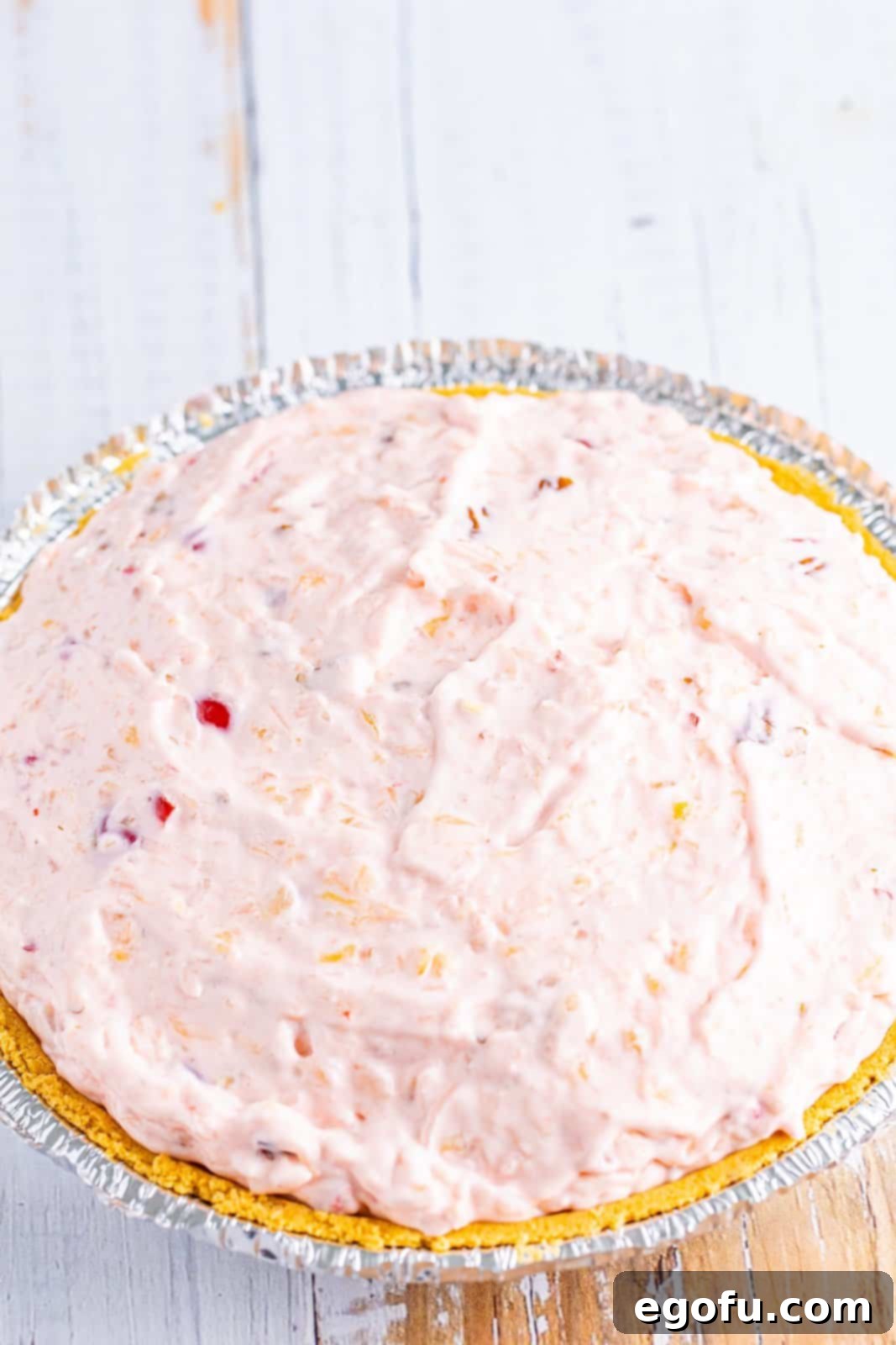 A delectable Millionaire Pie filling, rich with pineapple, cherries, coconut, and pecans, carefully smoothed into a golden brown graham cracker crust, ready for chilling.