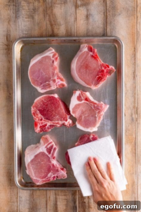 Soulful Mississippi Slow Cooker Pork 11 A baking sheet of pork chops with a hand patting them dry with a paper towel.