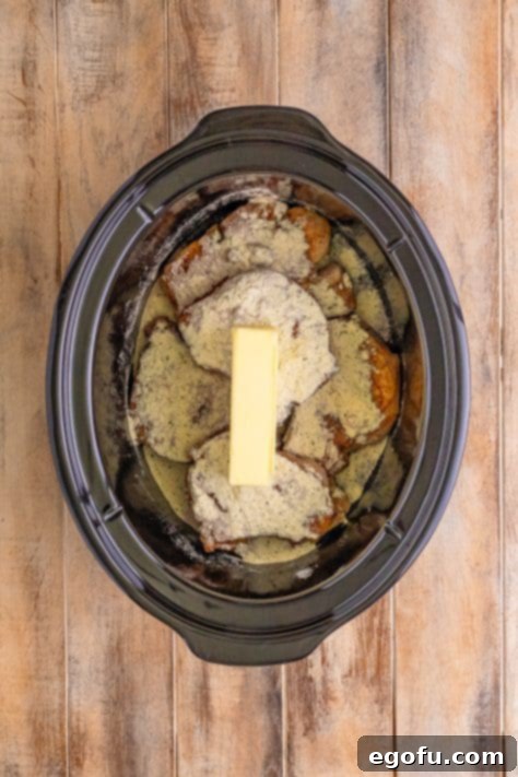 Soulful Mississippi Slow Cooker Pork 16 Slow cooker with pork chops, au jus, ranch seasoning, and a stick of butter placed on top.