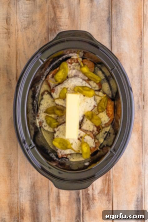 Soulful Mississippi Slow Cooker Pork 17 Slow cooker with pork chops, au jus, ranch seasoning, butter, and pepperoncinis scattered around.