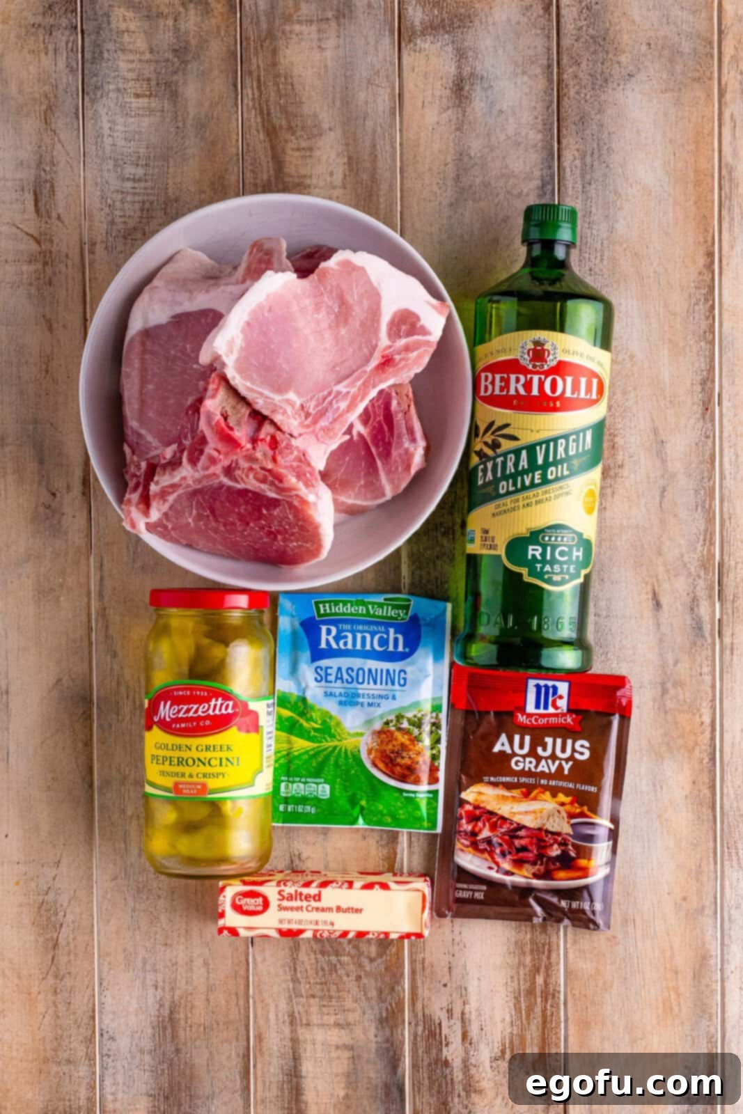 Soulful Mississippi Slow Cooker Pork 4 A collection of ingredients laid out: pork chops, olive oil, au jus gravy mix, ranch seasoning mix, pepperoncinis, and a stick of butter, ready for cooking.