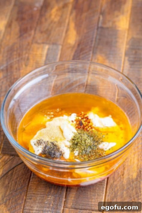 A mixing bowl with the mayonnaise, red wine vinegar, pepperoncini pepper juice, mozzarella ball marinade (from both containers) pepper, salt, oregano, garlic powder and red pepper flakes.