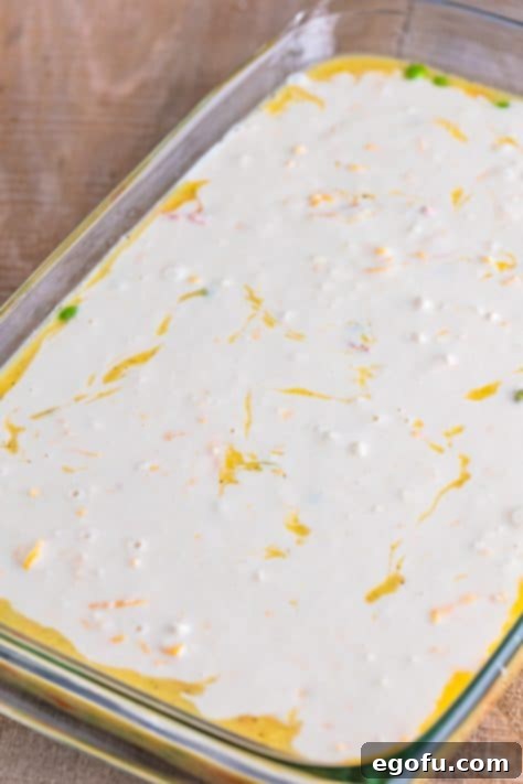 An unbaked Chicken Cobbler in a baking dish with biscuit topping spread.
