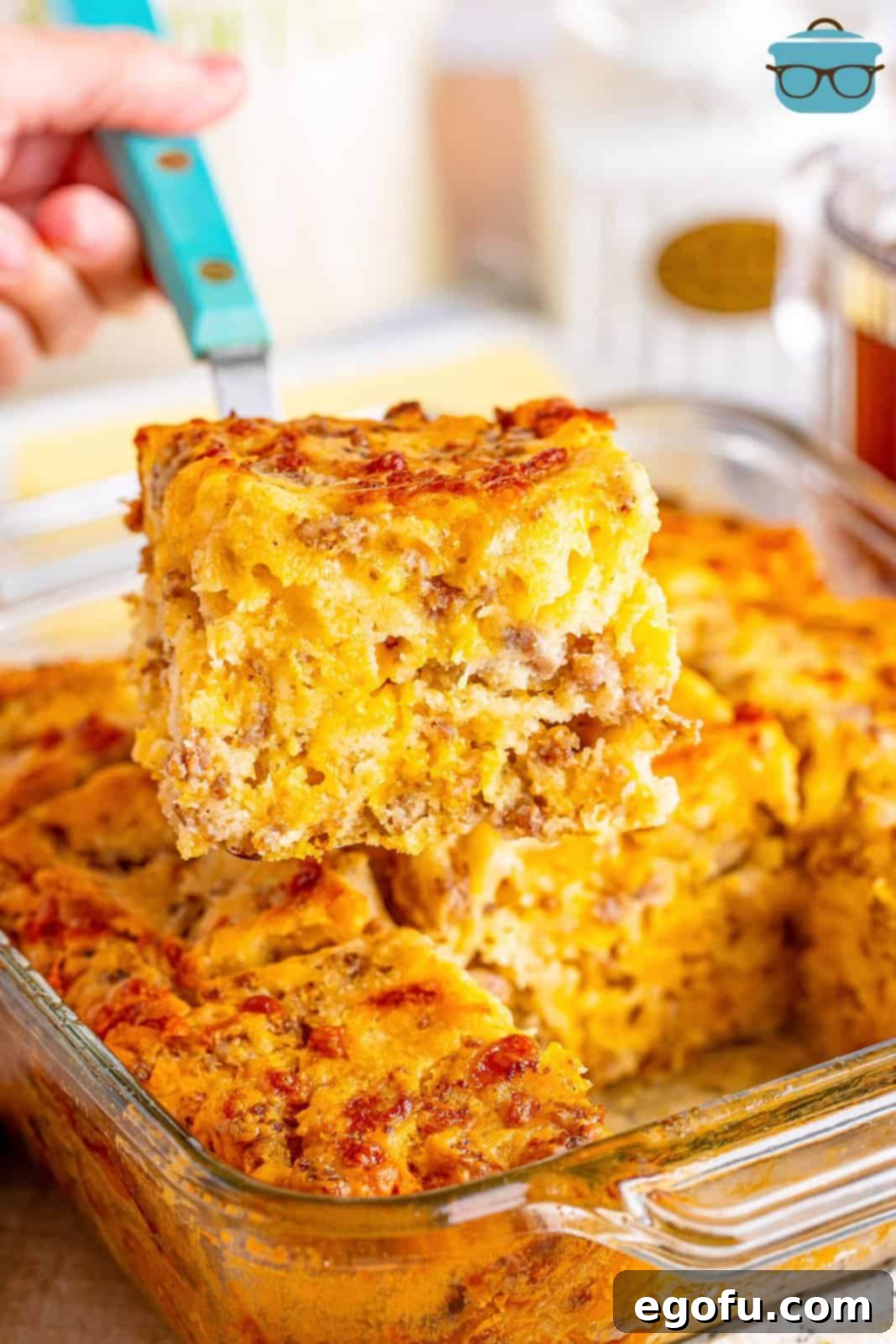 Serving utensil holding a breakfast butter swim biscuit above a baking dish.