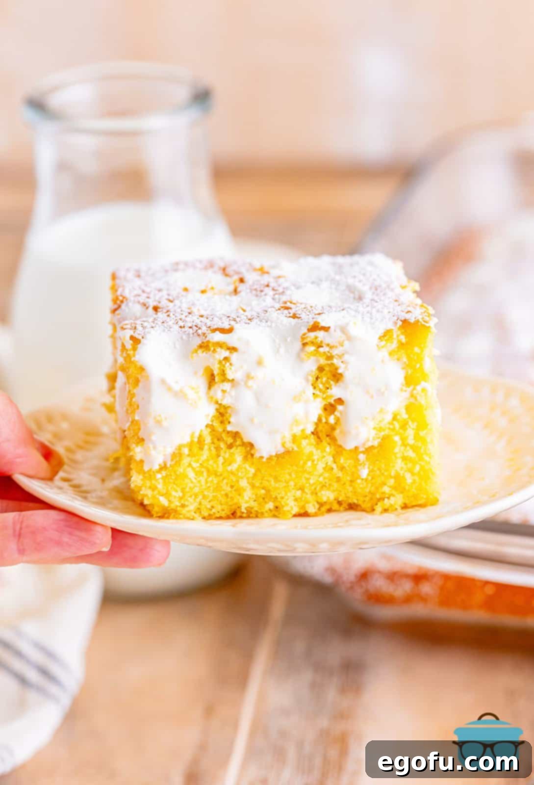 A hand holding a white plate showcasing a perfectly cut slice of Twinkie Poke Cake, revealing its golden layers and creamy filling.