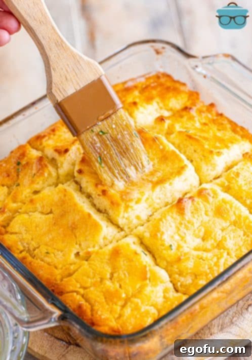 Garlic Butter Bath Biscuits 16 A pastry brush brushing garlic butter on warm biscuits in a baking dish.