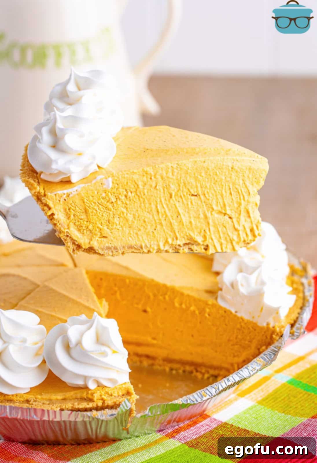 A slice of Pumpkin Cheesecake being held above the rest of the dessert by a serving utensil.