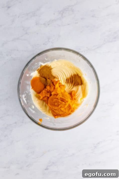 A mixing bowl with cream cheese, powdered sugar, pumpkin puree, pumpkin spice, and cinnamon.