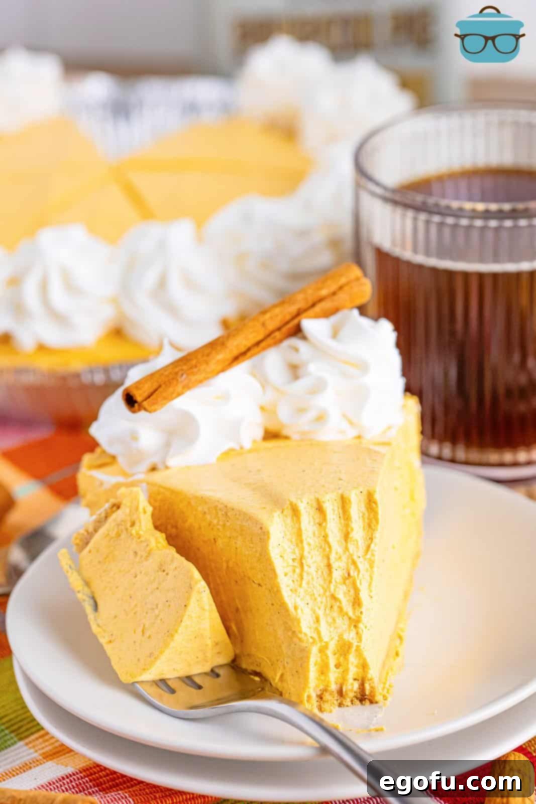 A fork holding a bite of No Bake Pumpkin Cheesecake next to the rest of the slice on a plate.