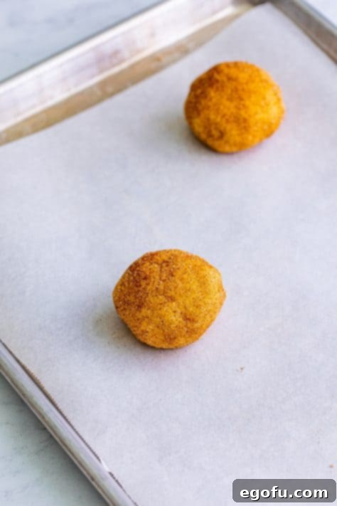 A parchment lined baking sheet with balls of cookie dough in them.