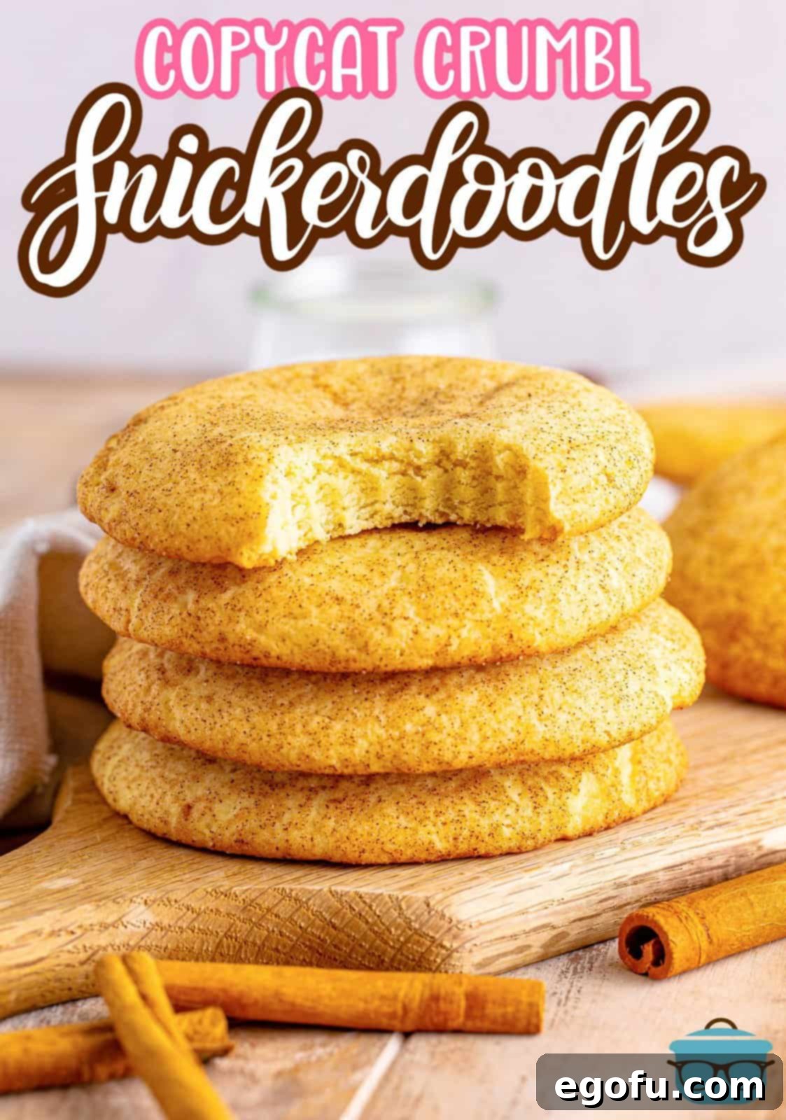 A trio of homemade copycat Crumbl Snickerdoodles stacked on a wooden surface, with one cookie having a bite taken out of it, revealing its soft interior.