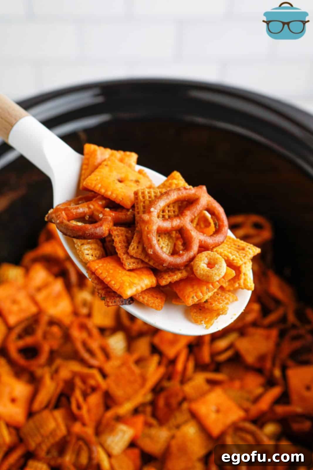 Ultimate Slow Cooker Buffalo Ranch Chex Mix 2 A spoon scooping a generous portion of freshly made Crock Pot Buffalo Ranch Chex Mix, highlighting its golden brown color and mix of textures.