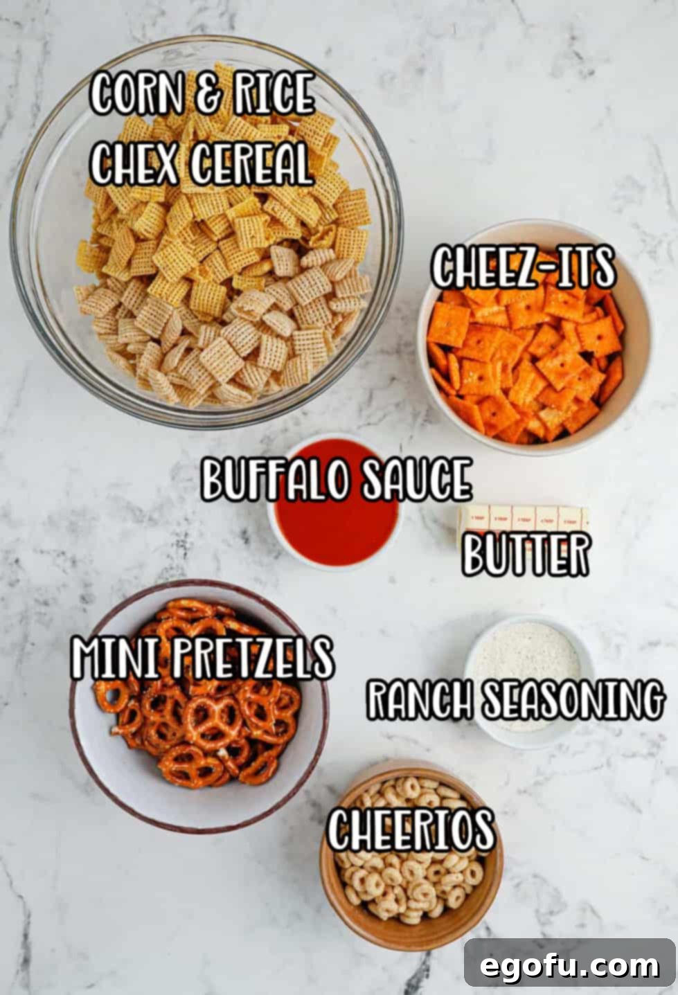 Ultimate Slow Cooker Buffalo Ranch Chex Mix 4 A flat lay of all the ingredients needed for Crock Pot Buffalo Ranch Chex Mix: rice and corn Chex cereal, Cheez-its, mini pretzel twists, Cheerios, a stick of butter, a bottle of buffalo sauce, and a packet of ranch seasoning.