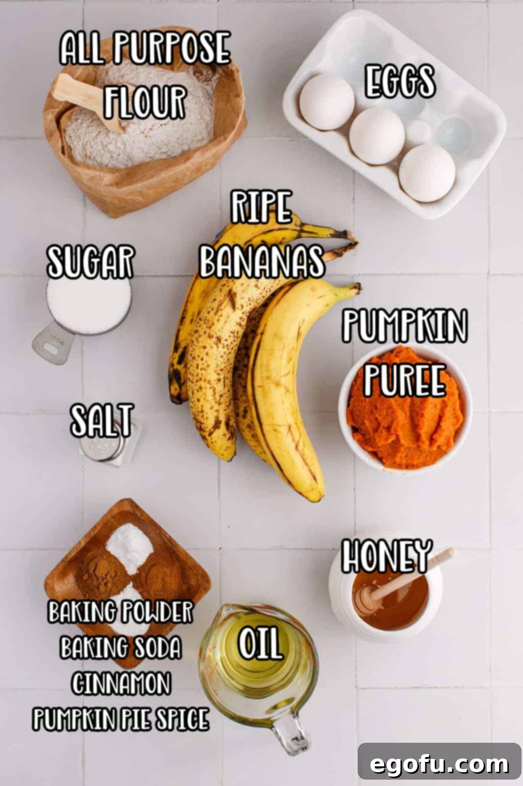 An array of ingredients laid out, including bananas, pumpkin puree, flour, pumpkin pie spice, ground cinnamon, baking powder, baking soda, salt, eggs, honey, sugar, and vanilla extract.