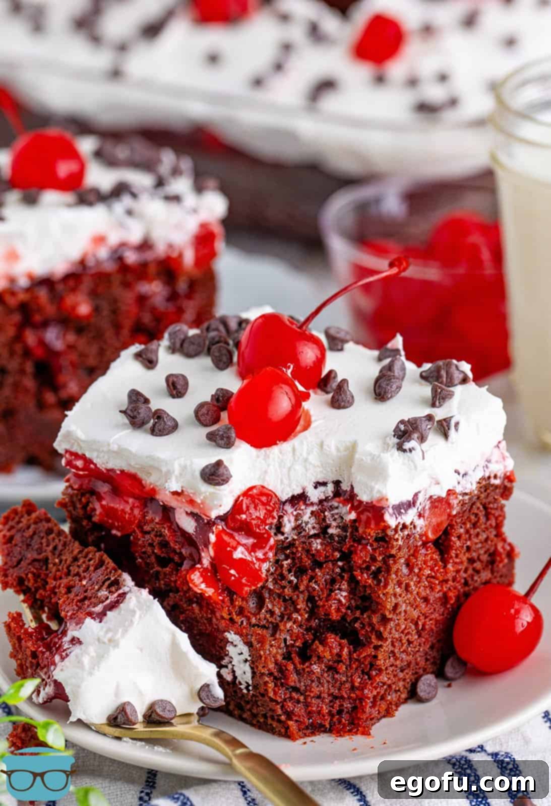 A beautifully garnished slice of Black Forest Poke Cake with a fork taking a bite.