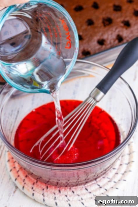Cherry Jell-O, a whisk, and cold water being poured into a mixing bowl.