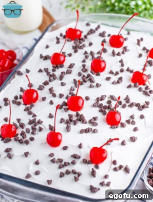 A Black Forest Poke Cake in the baking dish with chocolate sprinkles and cherries.