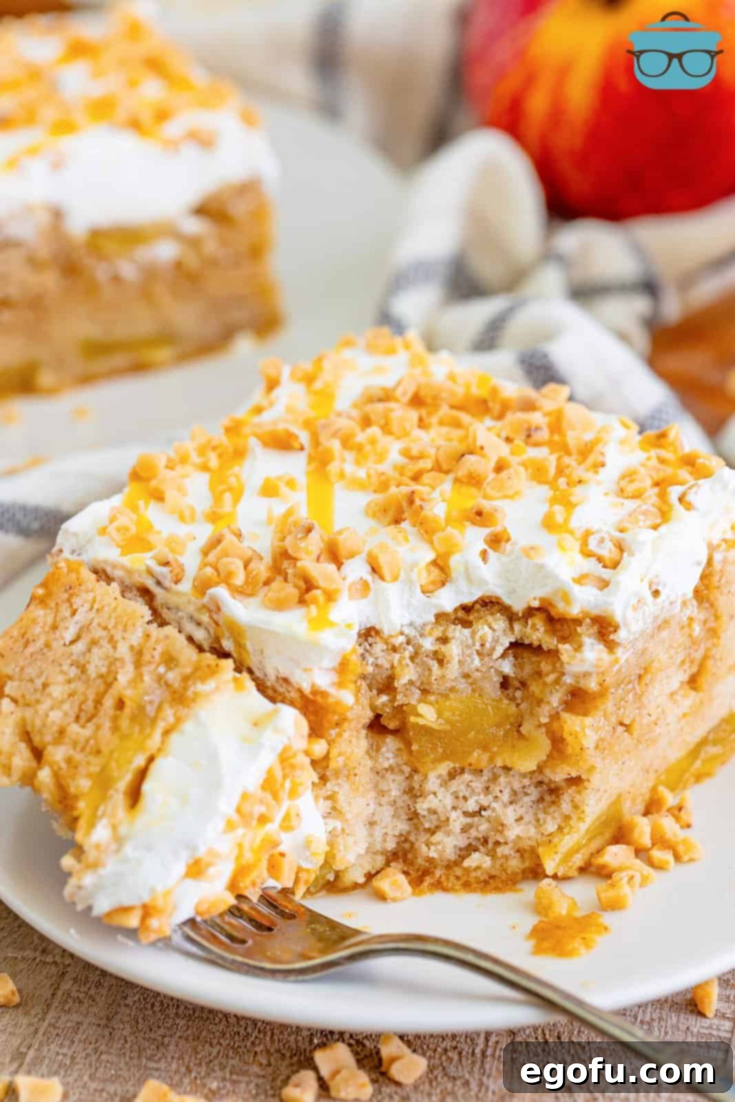 A white serving plate with a piece of apple pie poke cake and a fork with a bite of the cake on it.