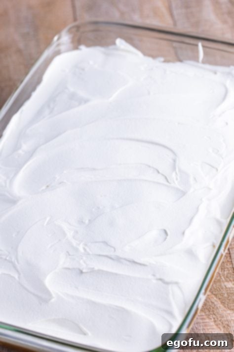 Whipped topping spread out over an Apple Pie Poke Cake.