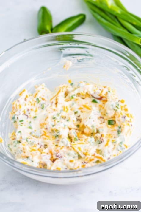 Mixing bowl with cream cheese, sour cream, cheese, bacon, jalapenos, and green onions.