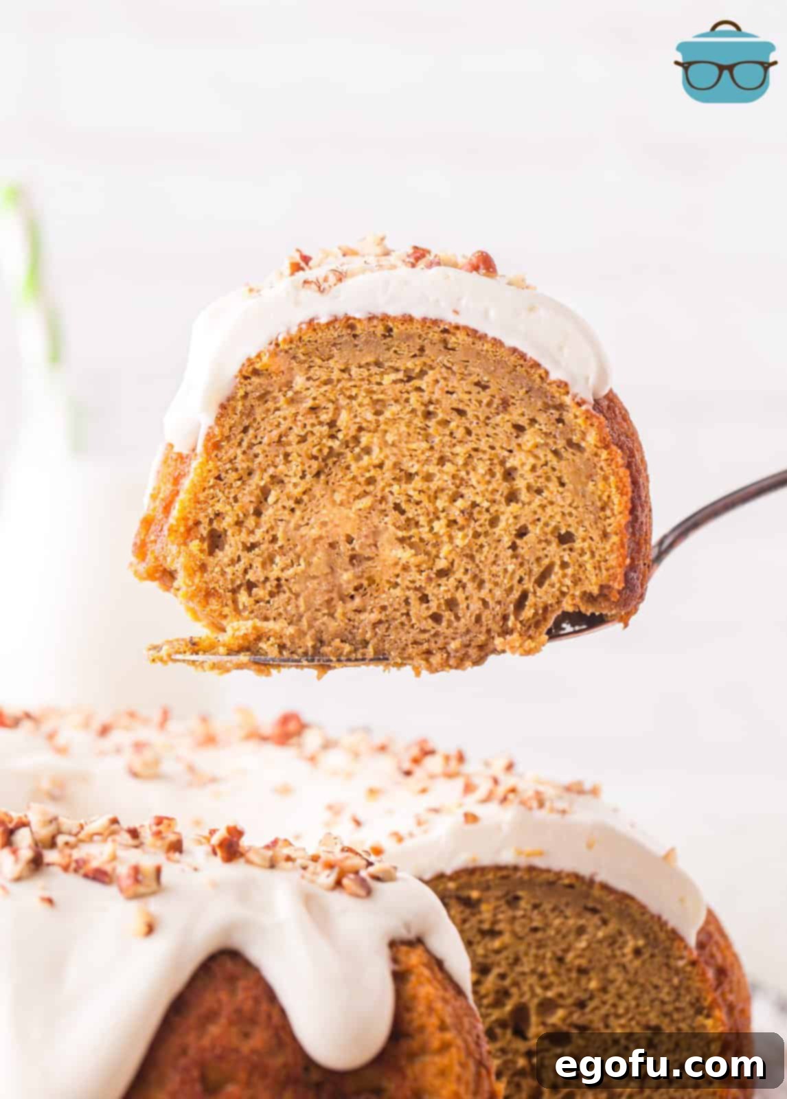 A serving utensil holding up a slice of glazed pumpkin Bundt cake.