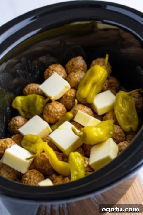 Cubed butter and pepperoncinis on top of meatballs in a Crock Pot.