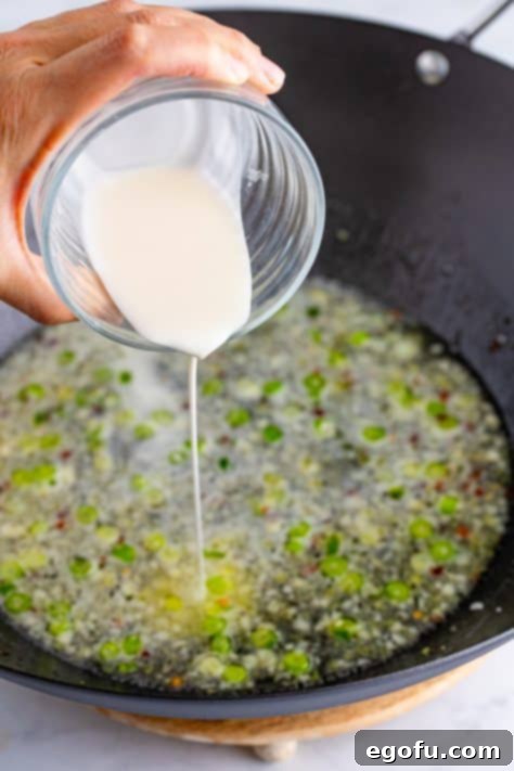 Cornstarch slurry being poured into a wok with other ingredients.