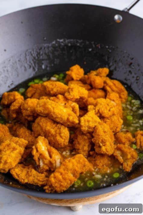 Popcorn chicken being added to a wok with other ingredients.